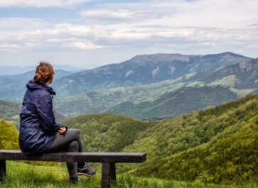 Woman sitting alone on a bench overlooking a mountain scene.