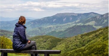 Woman sitting alone on a bench overlooking a mountain scene.