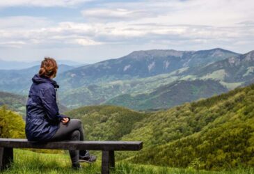 Woman sitting alone on a bench overlooking a mountain scene.