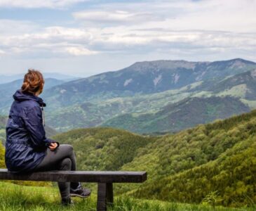 Woman sitting alone on a bench overlooking a mountain scene.